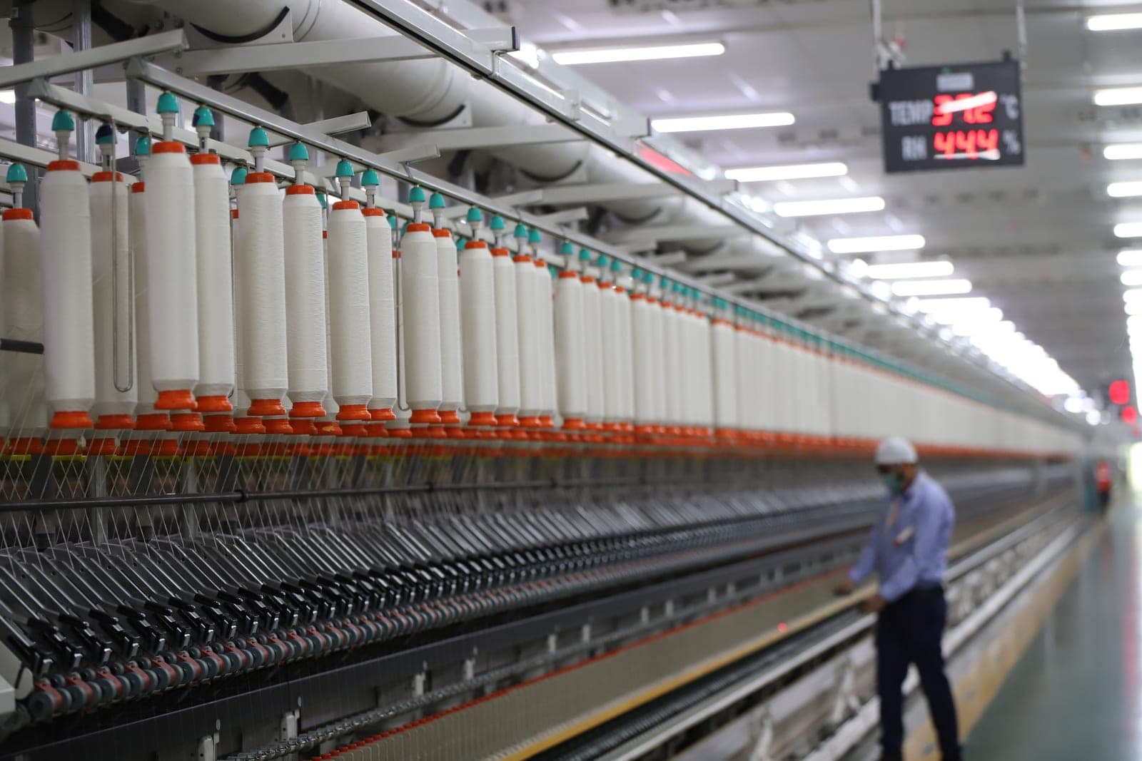 Ring spinning frame with rows of roving bobbins and a worker on a modern textile mill floor