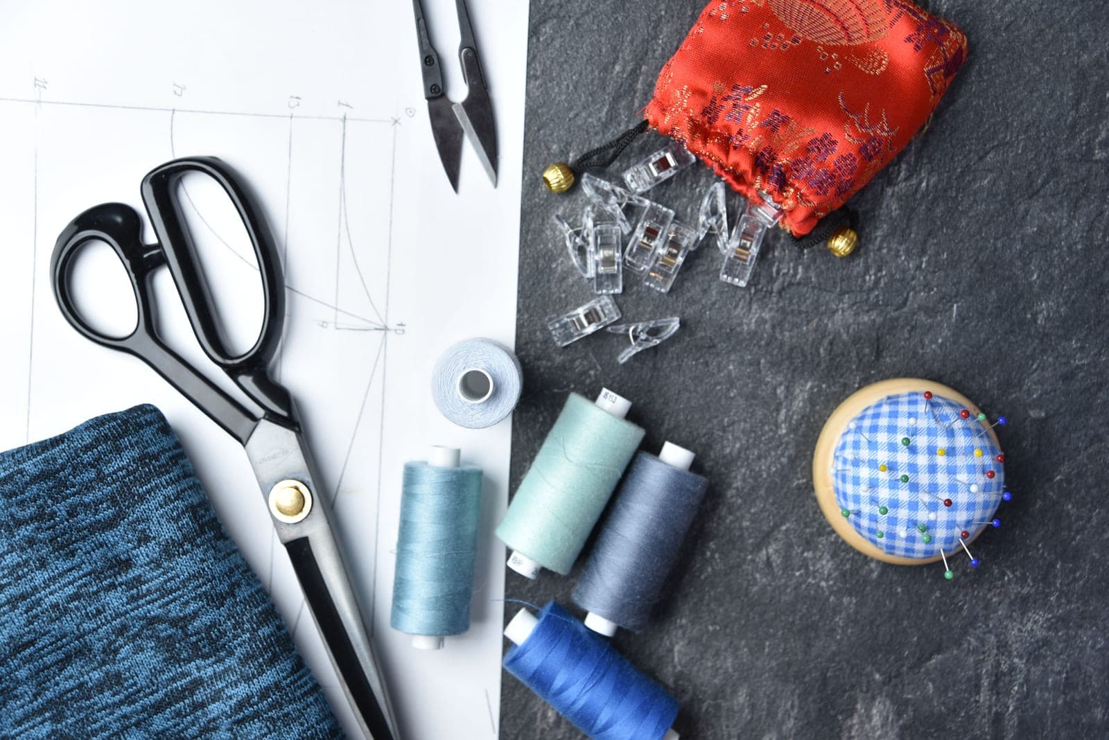 Flat lay of garment components — fabric, thread, scissors, clips and pins — that make up a bill of materials