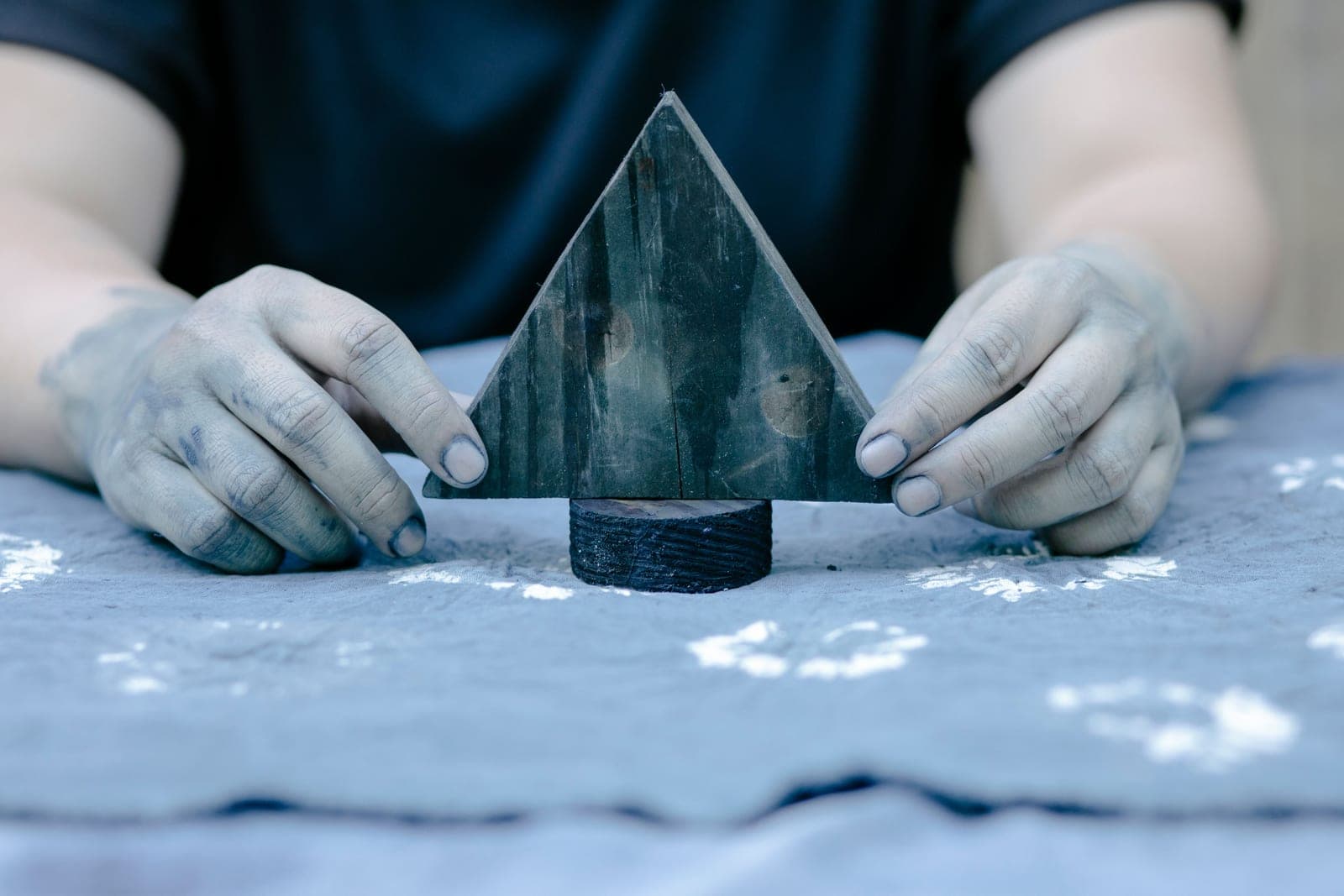 Artisan's dye-stained hands holding a carved wooden block over hand block-printed indigo fabric