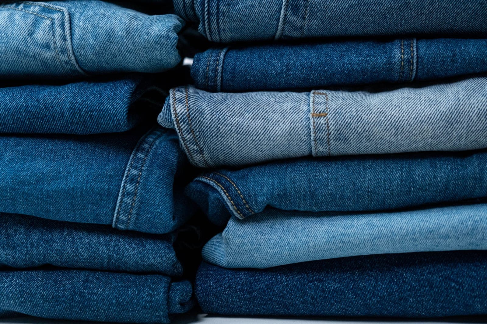 Stack of folded blue denim jeans in different wash shades from light to dark indigo
