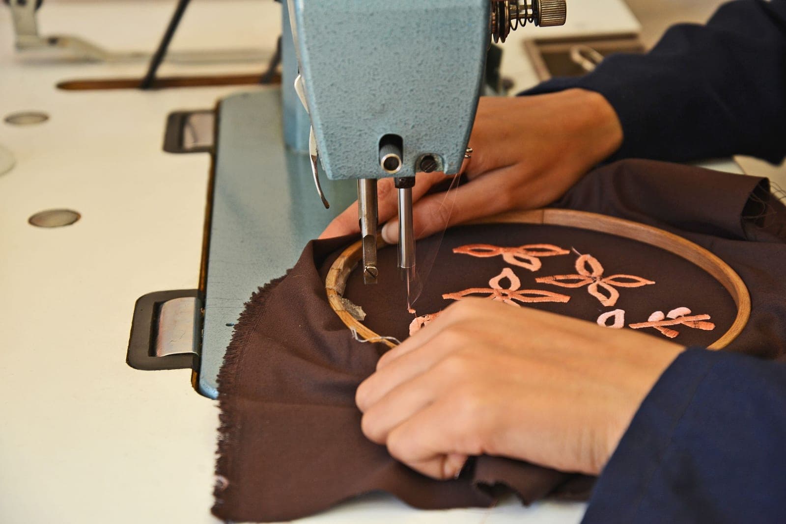 Hands embroidering a floral design on fabric with a hooped embroidery machine
