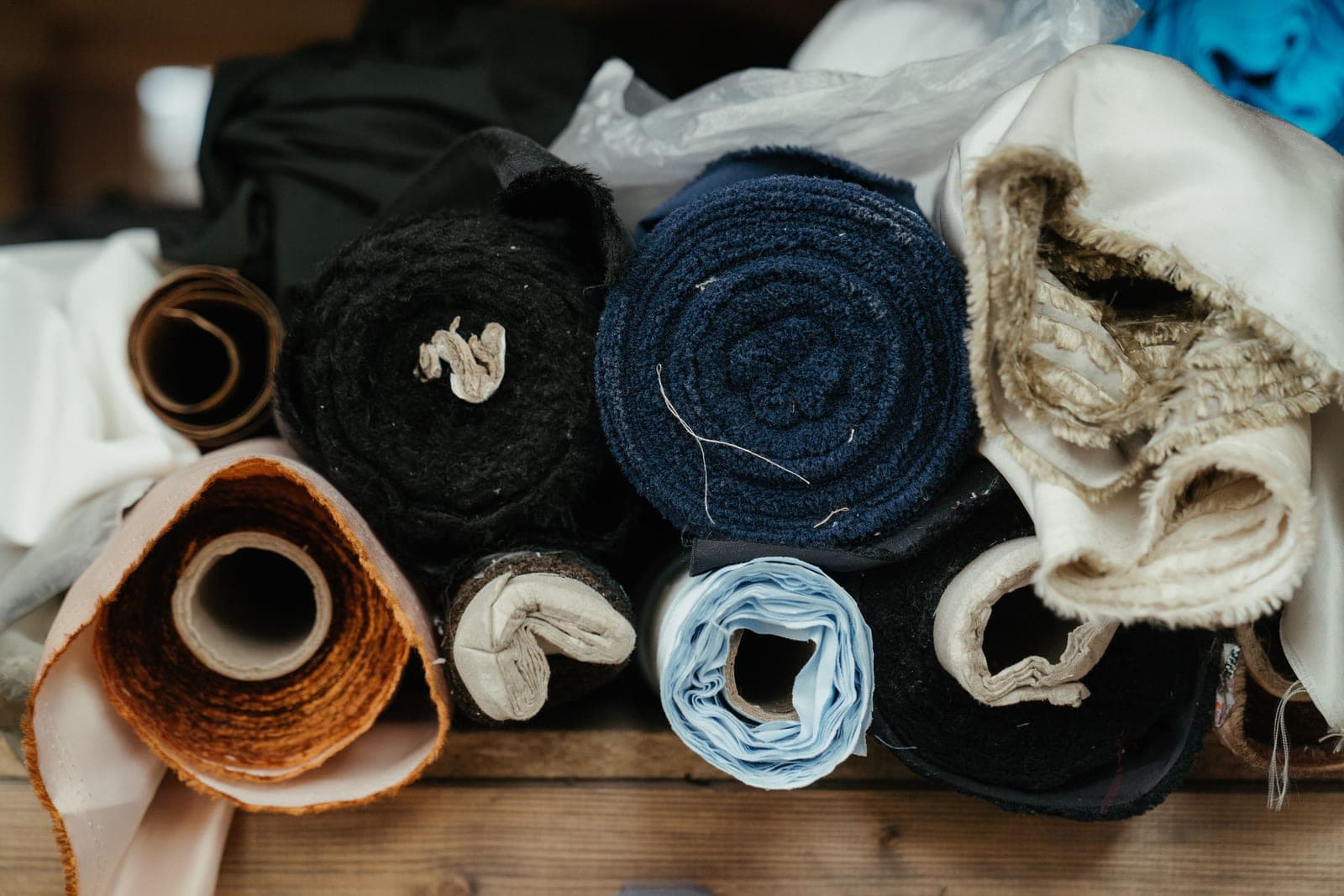 Rolls of finished fabric in different textures and colours stacked in a textile workshop