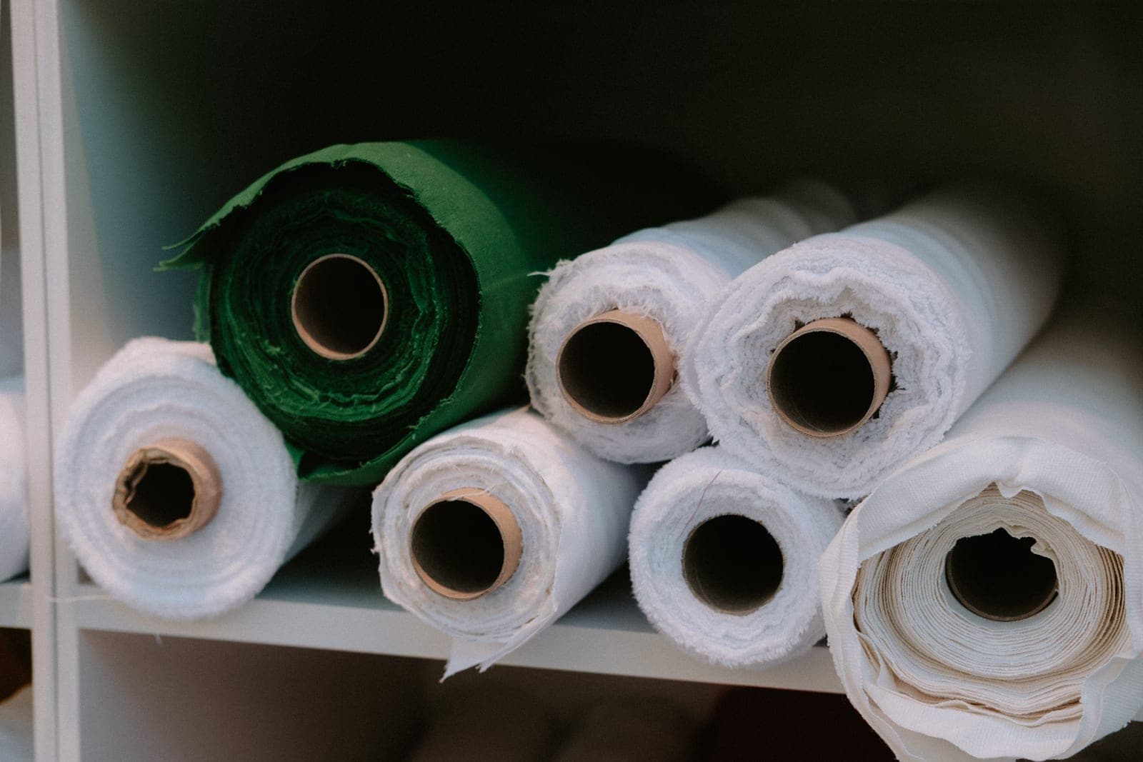 Rolls of fabric of different weights stacked on a shelf, illustrating GSM variation