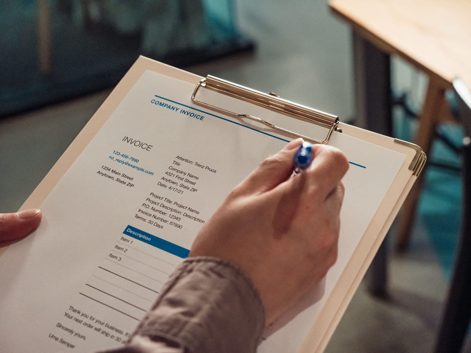 A hand reviewing a printed company invoice on a clipboard, the kind of document invoice processing automates