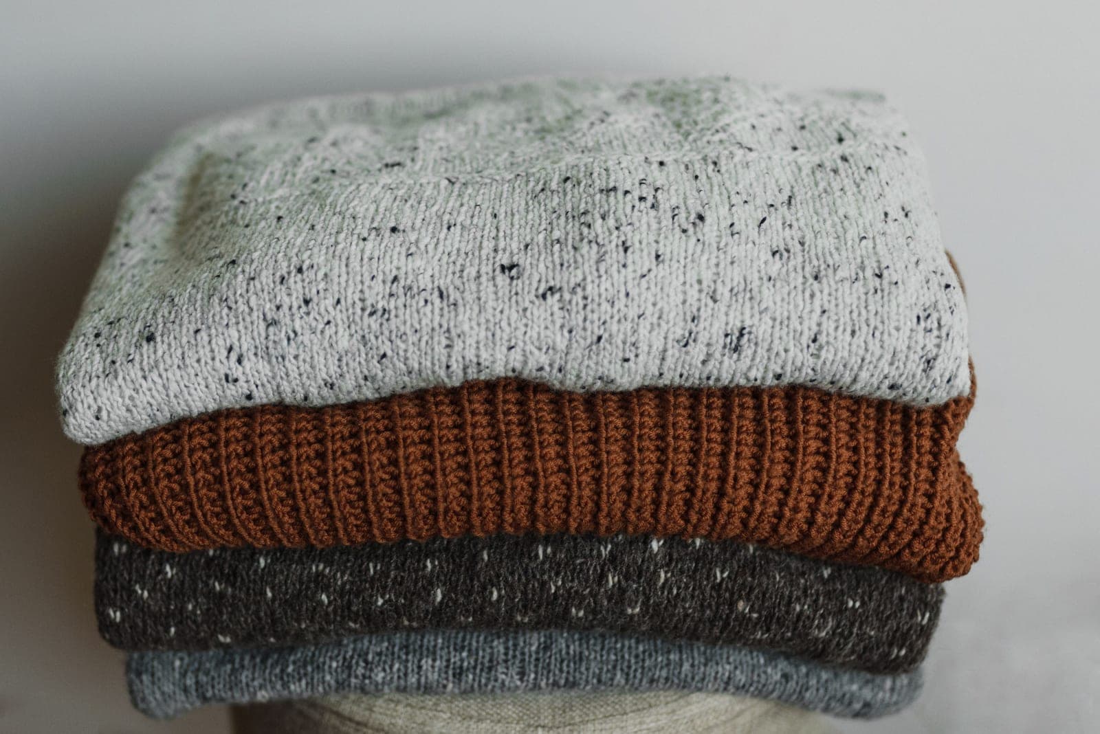 Stack of folded knitted sweaters in different textures and colours showing types of knitwear
