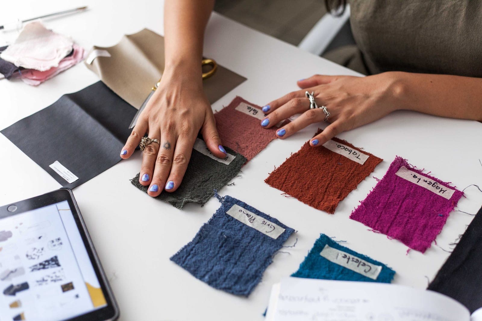Hands arranging labelled dyed fabric swatches beside a tablet while evaluating a lab dip
