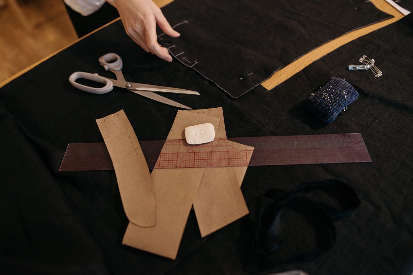Brown paper garment pattern pieces laid out on black fabric with shears and a ruler for marker making