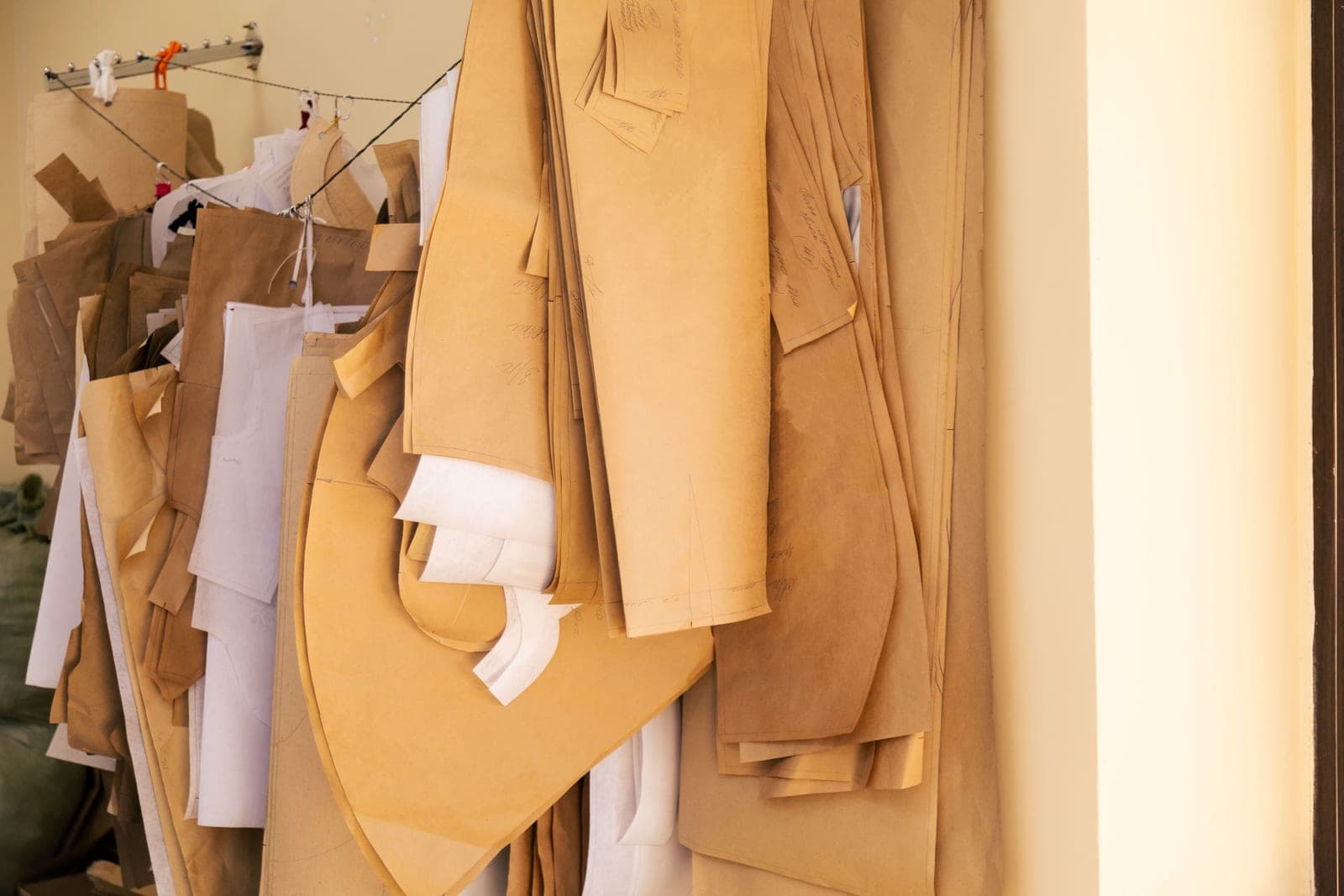 Brown paper garment pattern pieces in multiple sizes hanging on hooks in a pattern room