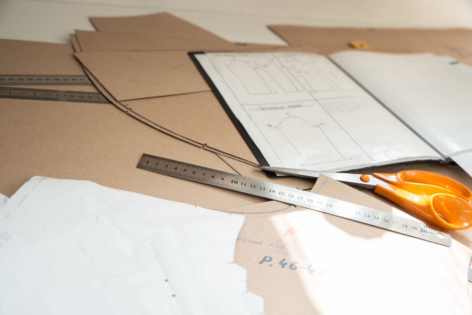 Paper garment pattern pieces with a ruler, scissors and a technical drawing on a pattern-making table