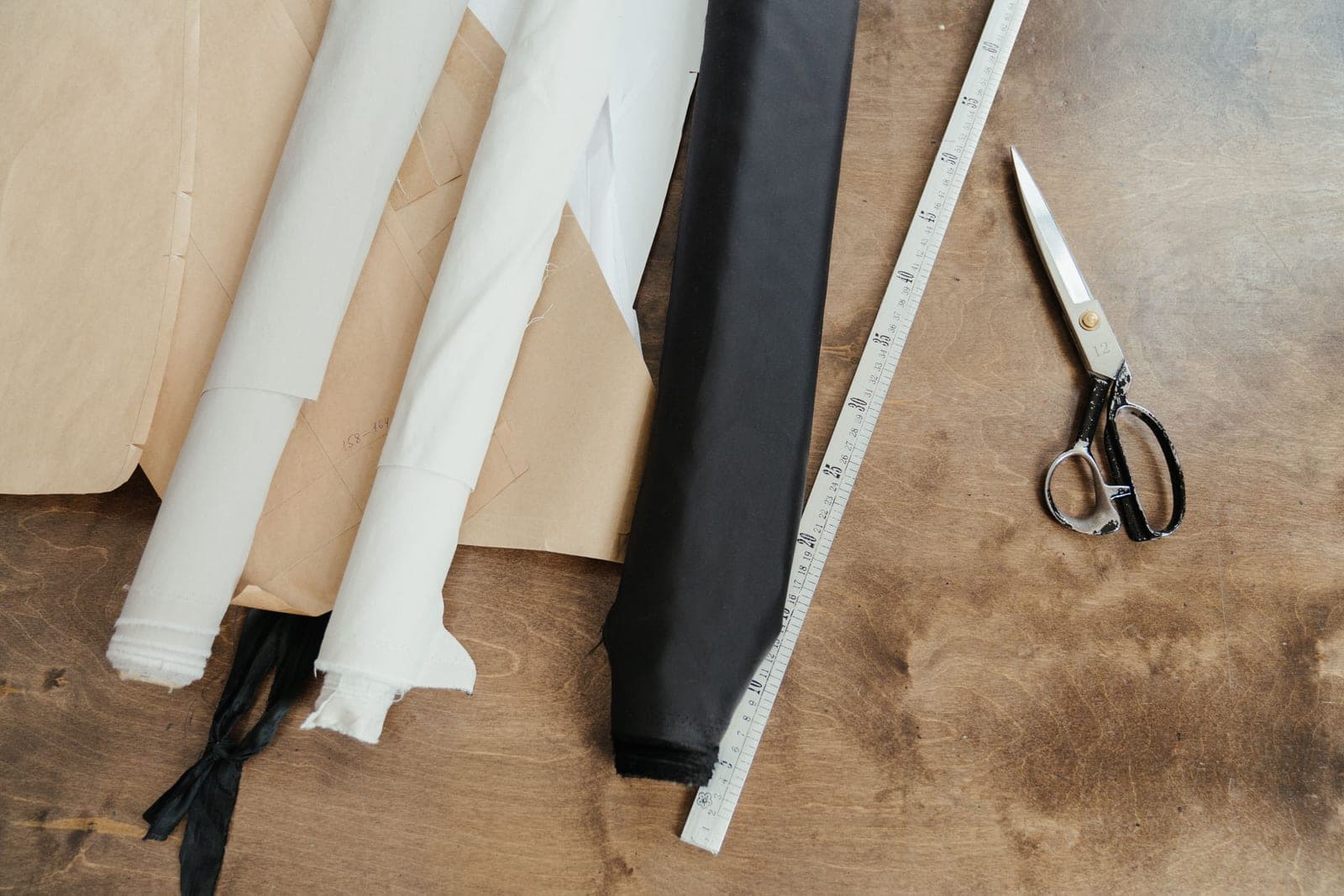 Rolls of fabric with a measuring tape and shears on a workbench, relating to fabric dimensions and shrinkage control