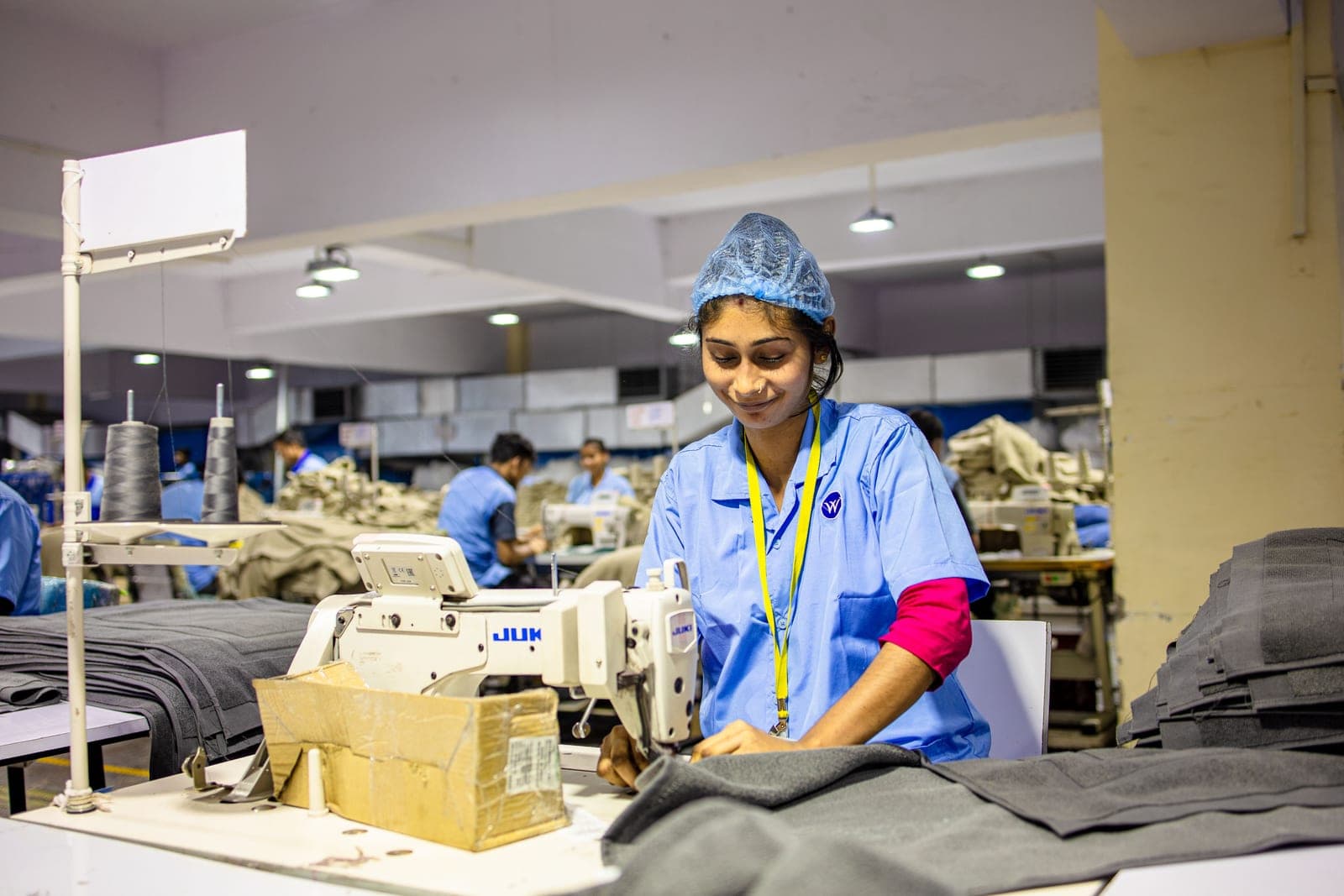 Garment factory worker sewing dark fabric at an industrial sewing machine with a sewing line behind