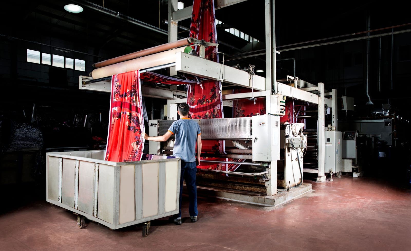 Worker operating an industrial textile printing machine with printed fabric running through it