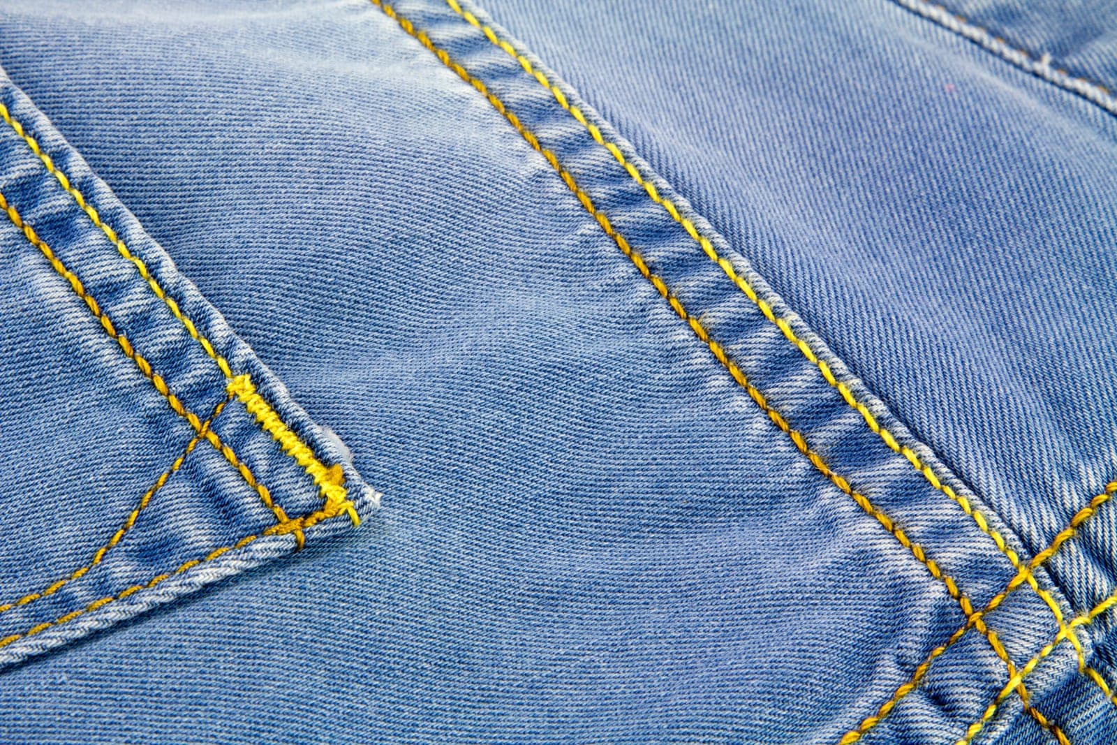 Close-up of blue denim showing the diagonal twill weave line and yellow topstitching