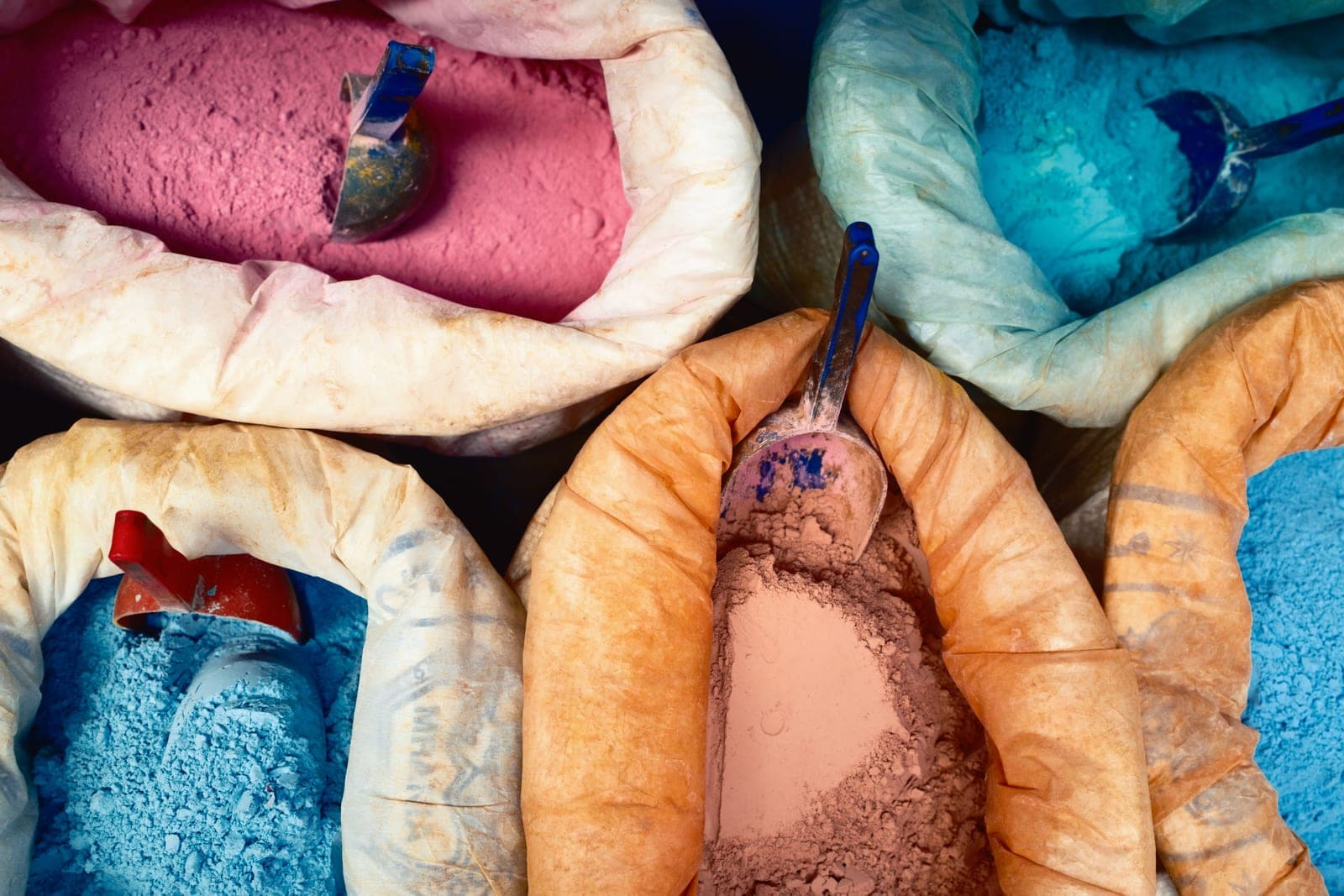 Open sacks of colourful textile dye powders in pink, blue, orange and tan with scoops