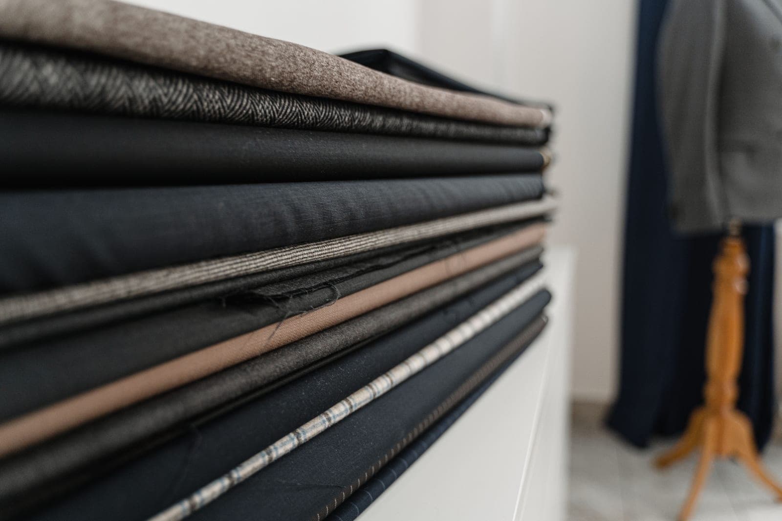 Stack of folded suiting fabrics in different weaves and textures showing several types of fabric