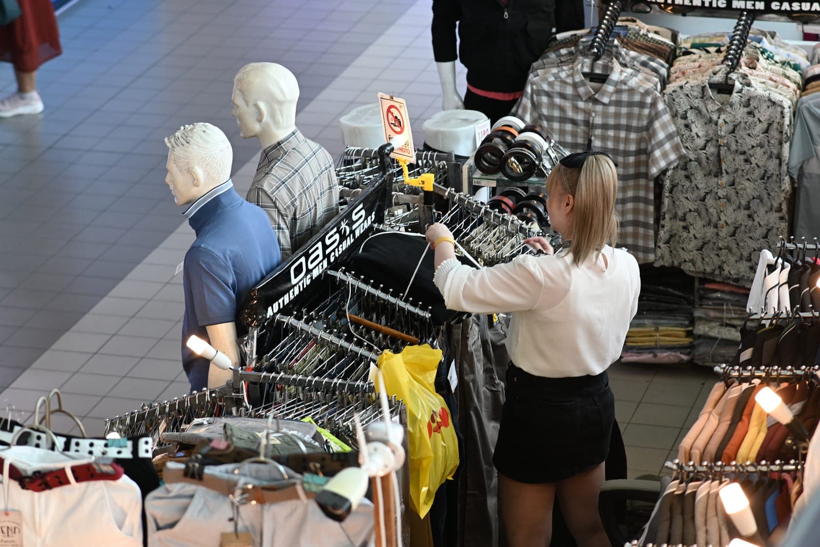 Customer browsing shirts on a clothing rack in a readymade garment store with folded stock
